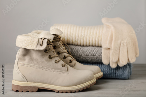 Leather women's light winter boots and a pile of knitted things (sweaters, scarves, gloves).