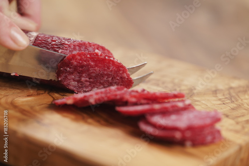 closeup female slicing thin salami sausage