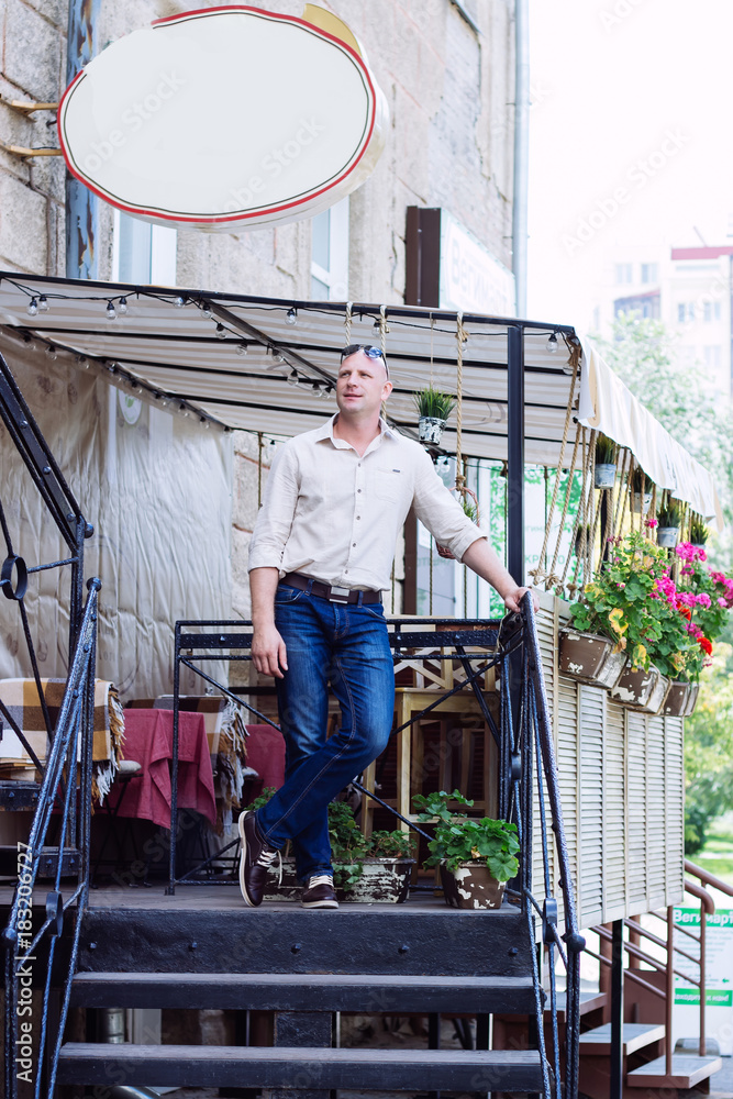 Handsome bald man is standing on the stairs on city european city at spring with cafe background. Summer.