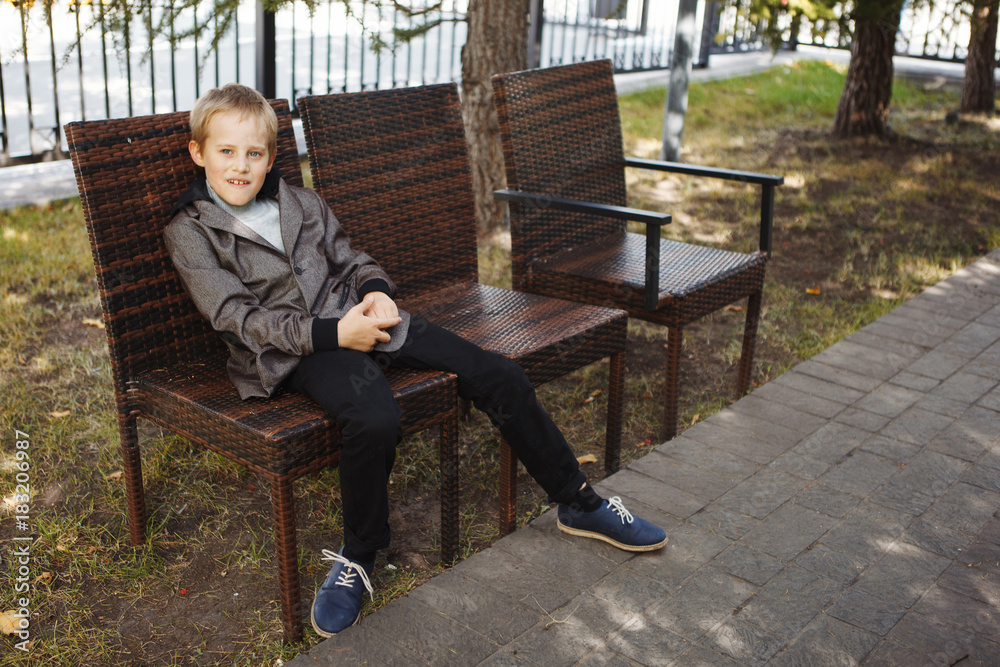 Handsome boy in a jacket, sitting on the bench looking at the Park on a Sunny fall day Handsome boy in a jacket, sitting on the bench looking at the Park on a Sunny fall day