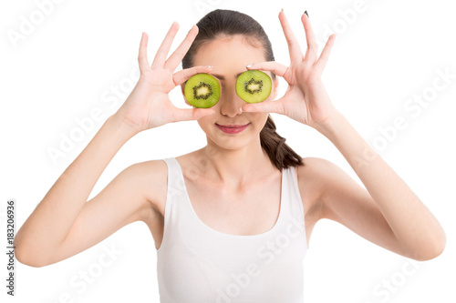 Beautiful woman holding kiwi slice hiding eye behind isolated on white background