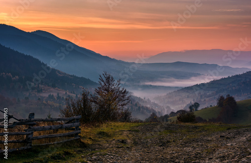 wooden fence on a slope of foggy valley at dawn. gorgeous landscape in forested mountains with red foliage