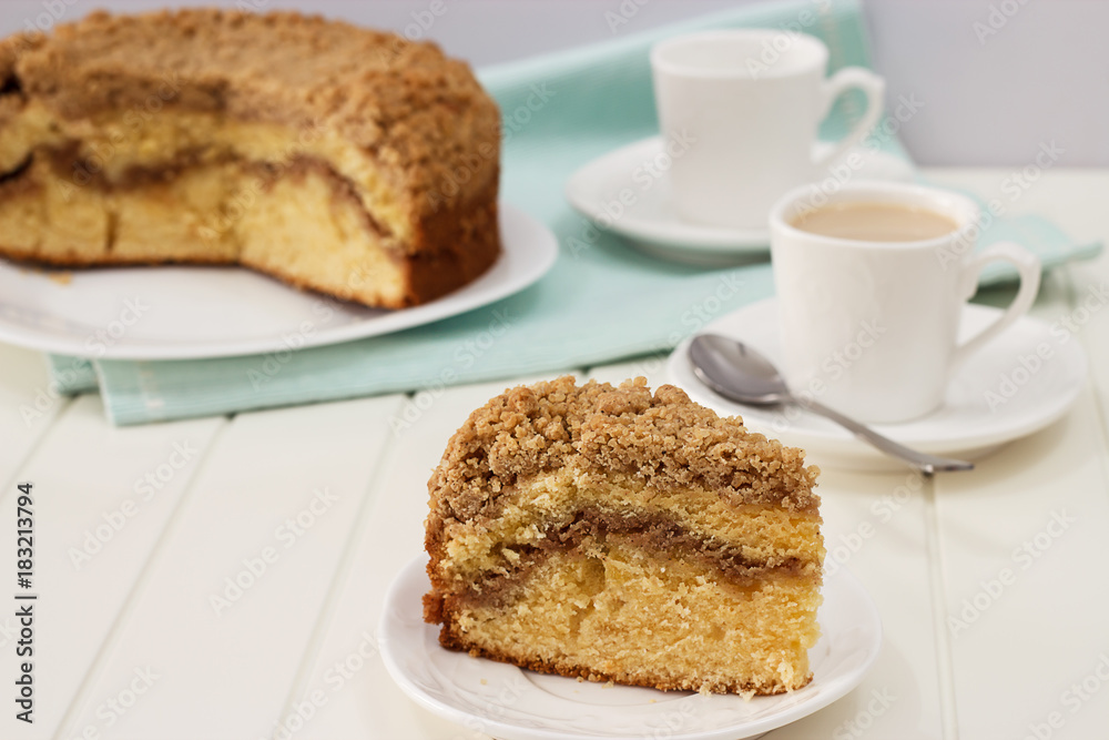 Close up piece of homemade Cinnamon crumble coffee cake and cup of milk tea. White wooden background.