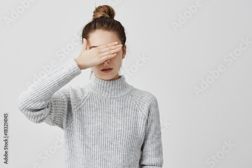 Skinny woman wearing grey outfit closing her eyes with hand. Confident female trying to hide her face from other people prefer not to see. Decision, human concept