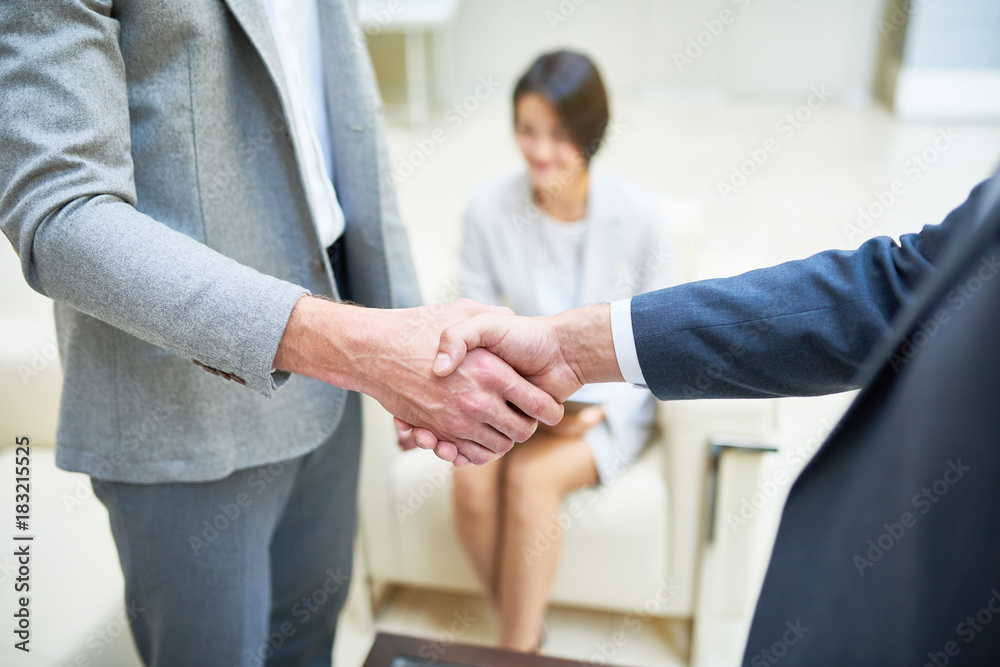 High angle close up of two successful businessmen shaking hands during meeting after closing important deal, young Asian woman in background High angle close up of two successful businessmen shaking hands during meeting after closing important deal, young Asian woman in background