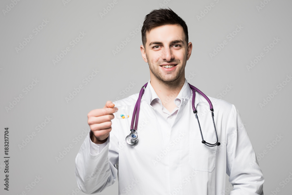 Smiling doctor offering a cup of pills or drugs on gray background. Daily medicine, dose or vitamins concept Smiling doctor offering a cup of pills or drugs on gray background. Daily medicine, dose or vitamins concept