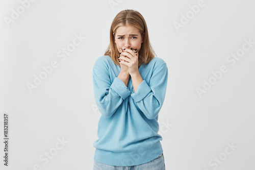 Close up shot of upset teenage girl wearing blue sweater and jeans almost crying, hiding her face, absolutely shocked with the bad news.