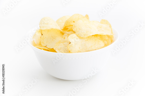 Crispy thinly sliced potato chips in white bowl, on white background.