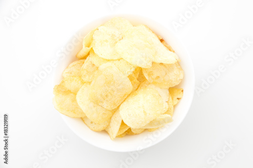 Crispy thinly sliced potato chips in white bowl, on white background.