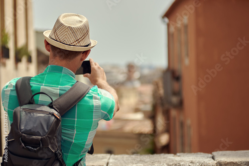 Male traveler in sunhat is taking a photo of a view with mobile phone.