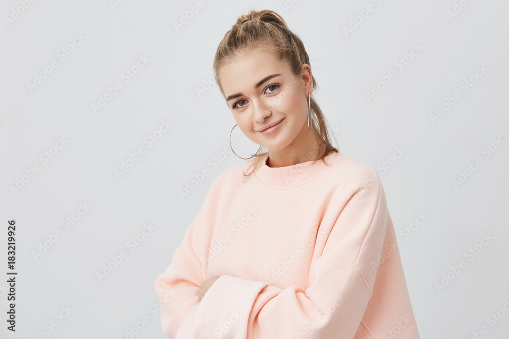 Charming good-looking stylish european girl loking with her dark eyes at camera, smiling at camera, wearing pink sweatshirt with big round earings. Beauty and youth concept. Charming good-looking stylish european girl loking with her dark eyes at camera, smiling at camera, wearing pink sweatshirt with big round earings. Beauty and youth concept.