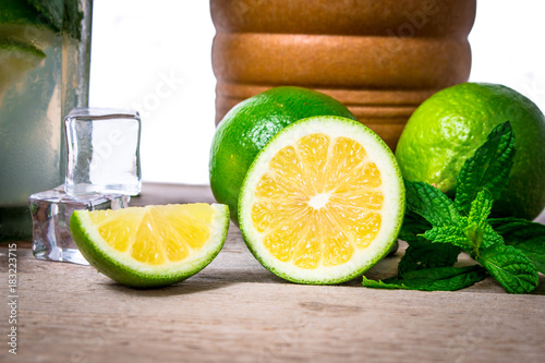 Mojito cocktail with ingredients. Fresh lime, mint leaves and ice cubes, morter with mint and brown sugar on a wooden background. Refreshing alcohol drink. Isolated on white background..
