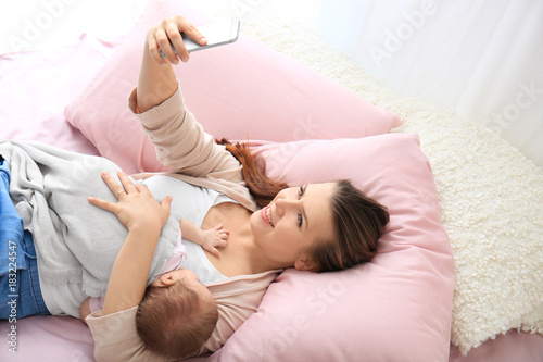 Young mother taking selfie with baby on bed at home