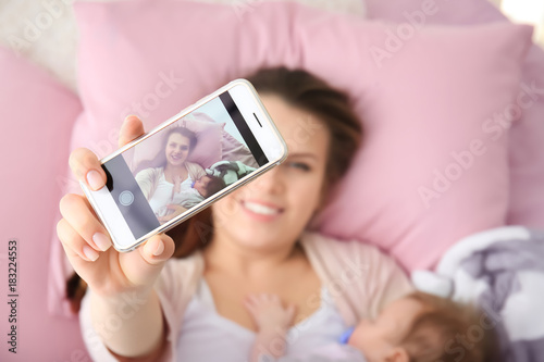 Young mother taking selfie with baby on bed at home