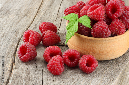 ripe raspberries in wooden bowl on old wooden table background
