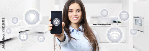 smart home smiling woman showing cell phone screen with symbols on kitchen and living blurred background