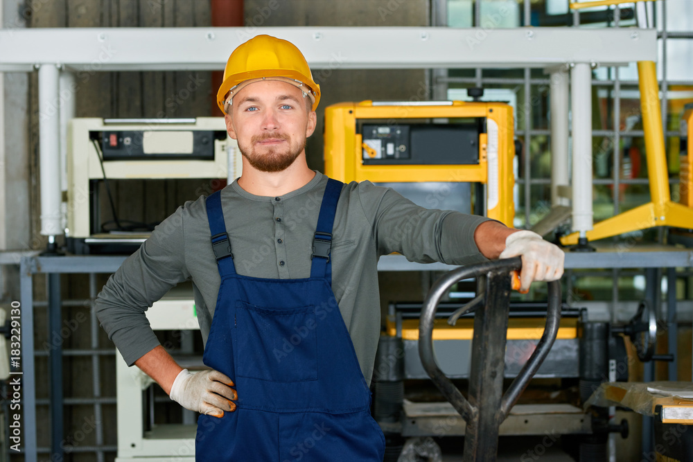 Portrait of cheerful young worker wearing hardhat posing looking at camera while working at modern factory workshop Portrait of cheerful young worker wearing hardhat posing looking at camera while working at modern factory workshop