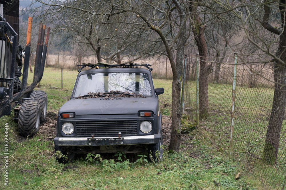 Retro and vintage russian and soviet vehicle in the garden and countryside. Bare trees are behind off-road car. Dull and muted colors during autumn and fall.
