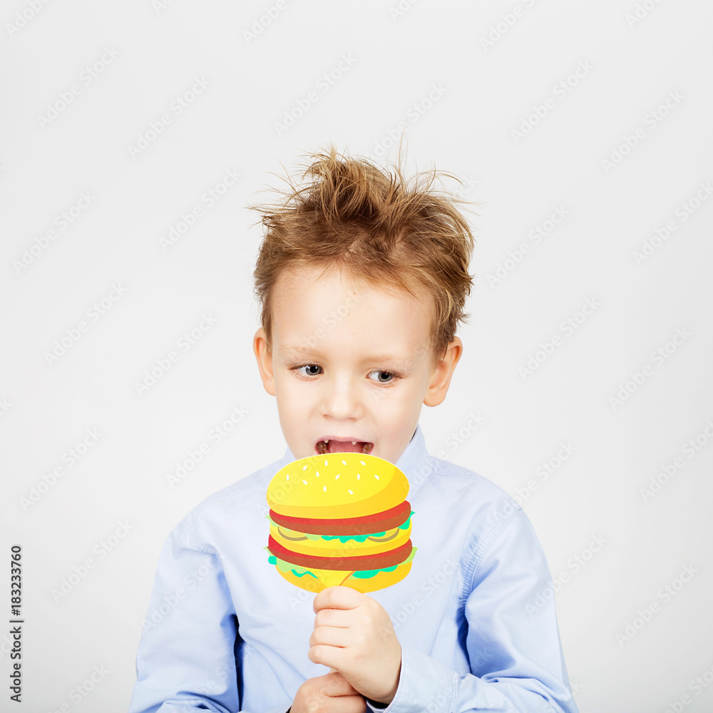 Cute little school boy with fake paper burger against a white background. Cheerful smiling Kid with funny photo props. unhealthy food concept. Back to School. Cute little school boy with fake paper burger against a white background. Cheerful smiling Kid with funny photo props. unhealthy food concept. Back to School.