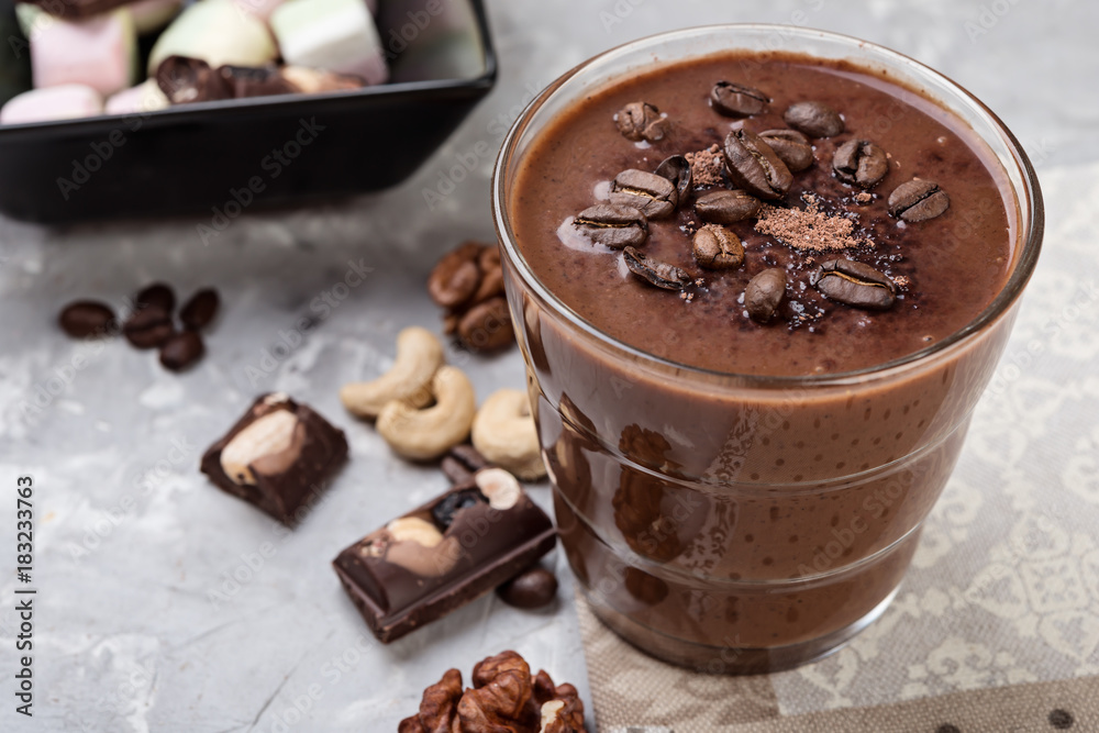 Chocolate smoothie on a glass with coffee beans and nuts on grey stone background Chocolate smoothie on a glass with coffee beans and nuts on grey stone background