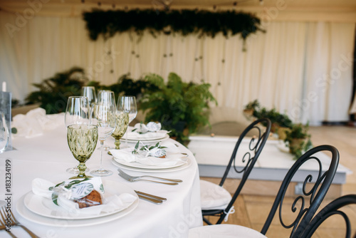 Decorated tables with plates, knives, forks and bouquet with white flowers and greens on the centre