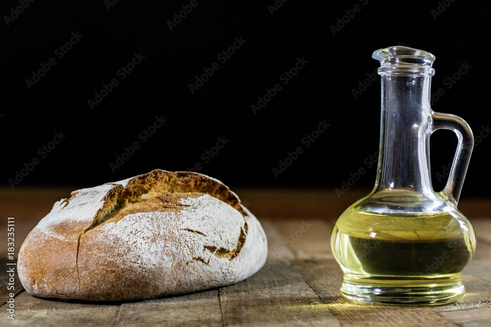 Obraz premium Tasty country bread and olive oil in a glass bottle. Wooden table.
