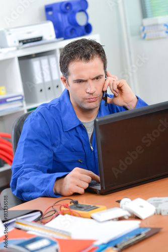 Man in overalls on computer, frowning