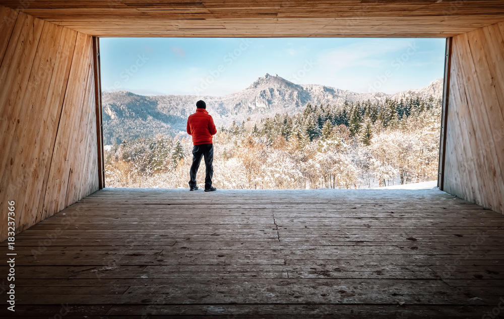 Man stay in big wooden hangar and looks on snowy mountains - obrazy, fototapety, plakaty 