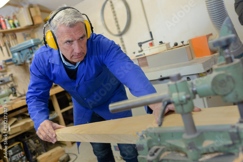 senior carpenter using bandsaw to cut wooden plank in workshop