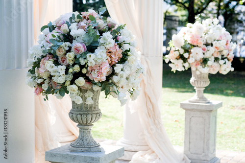 White wedding arch with big peach bouquets on the white stands