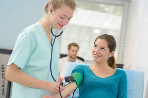 young female doctor with a stethoscope taking pressure of patient photo