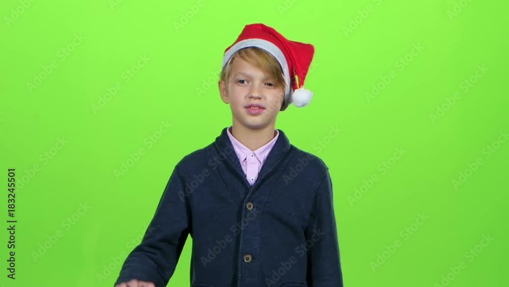 Child boy in the cap of santaclaus raises his hand and shows the card on a green screen. Slow motion Child boy in the cap of santaclaus raises his hand and shows the card on a green screen. Slow motion