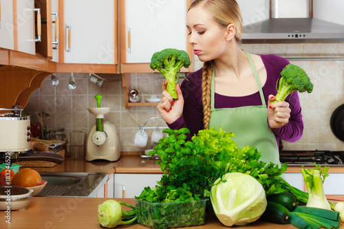 Woman in kitchen with green vegetables broccoli in hand