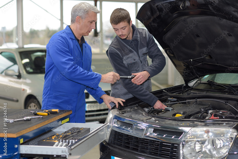student mechanic learning from teacher in automotive vocational school