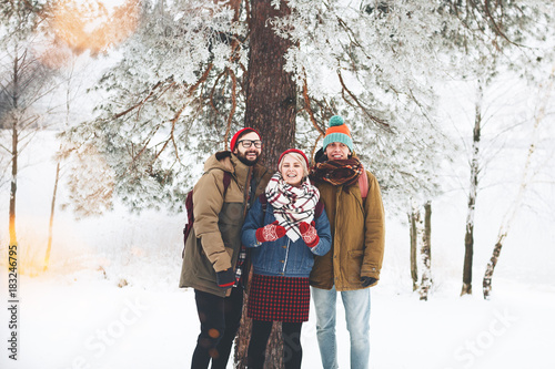 Happy and joyful friends in warm and cozy clothes walk through the winter forest. Сompany of guys and girls are having fun together in a snowy landscape