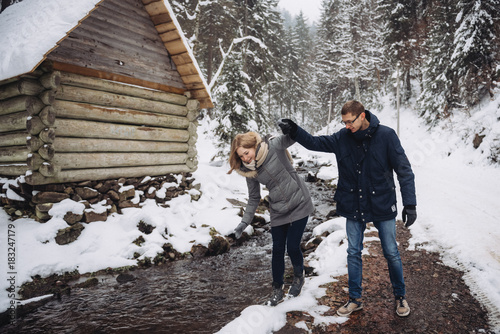 Young beautiful couple hold hands and having fun near the winter mountain river © blackbirdua