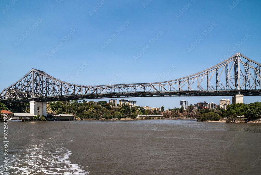 Brisbane, Australia - December 8, 2009: Iconic historic metal Story Bridge over the river seen from on the brownish water under clear blue sky. Part of city skyline.