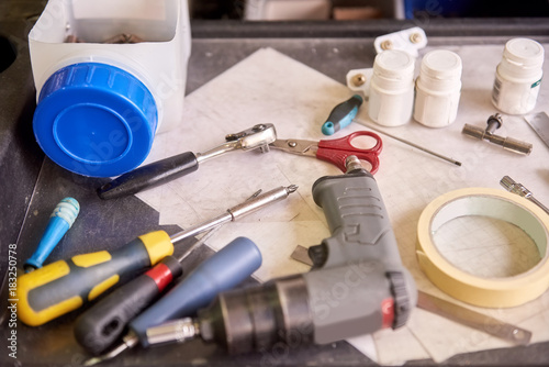 Large amount of tools are lying on a metal plate. Electric srewdriver, hand screwdriver, insulating tape, scissors and containers. photo