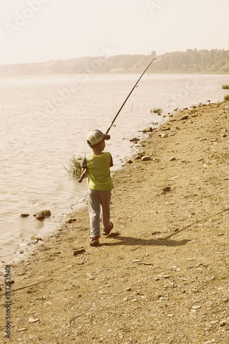 little boy walks with a fishing rod along the shore to fish early morning