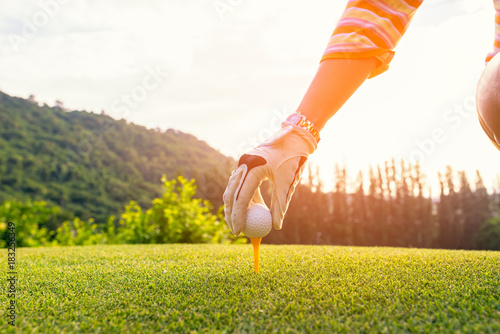 Hand asian woman putting golf ball on tee with club in golf course on sunny day for healthy sport. Lifestyle Concept