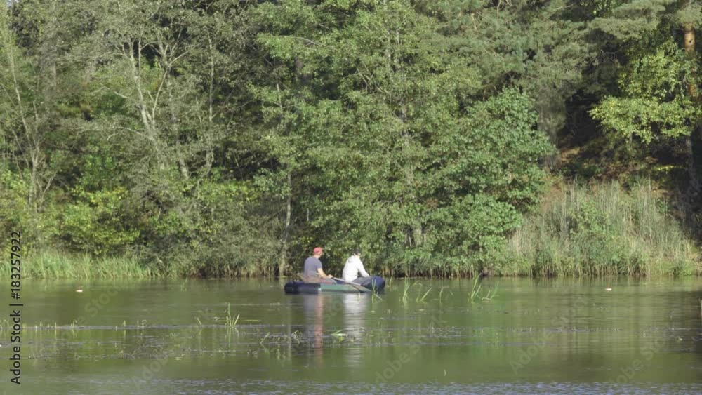 Two fisherman in rubber boat floats rowing with oars on river. Man is fishing on lake in sunny forest. Stracha river - beautiful place close to Belarusian nuclear power plant Two fisherman in rubber boat floats rowing with oars on river. Man is fishing on lake in sunny forest. Stracha river - beautiful place close to Belarusian nuclear power plant