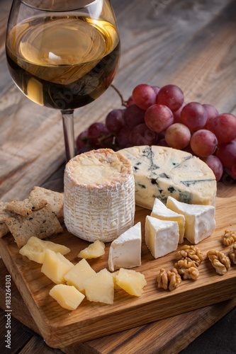 Tasting cheese dish on a wooden plate. Food for wine and romantic, cheese delicatessen on a wooden rustic table.