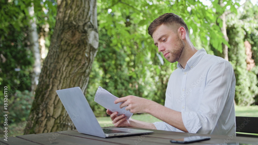 A young man reading and using a laptop and in the park. Medium shot. Soft Focus A young man reading and using a laptop and in the park. Medium shot. Soft Focus