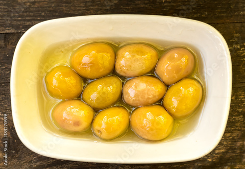 old wooden table and top view of big green olives in a plate