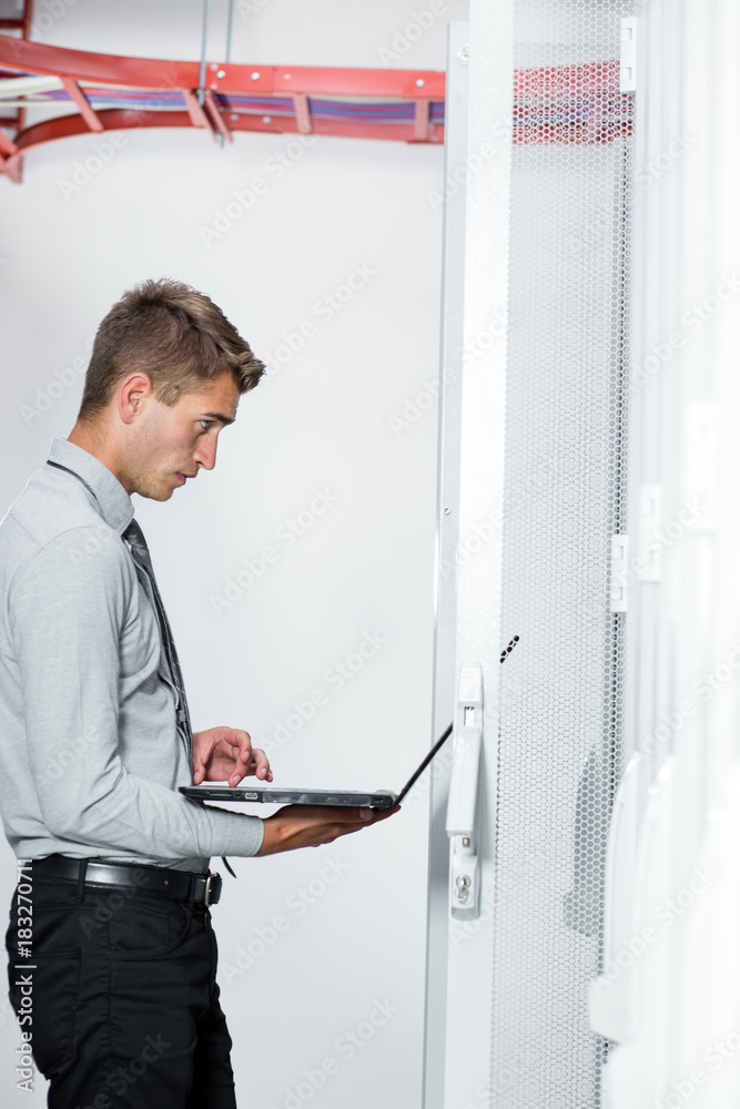 Portrait of modern young man holding laptop standing in server room working with supercomputer Portrait of modern young man holding laptop standing in server room working with supercomputer