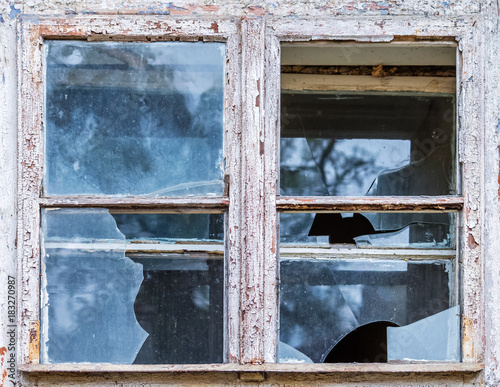 The old window of an abandoned house with shabby paint and dirty, broken glass