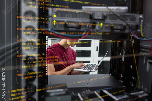 Portrait of modern young man holding laptop standing in server room working with supercomputer