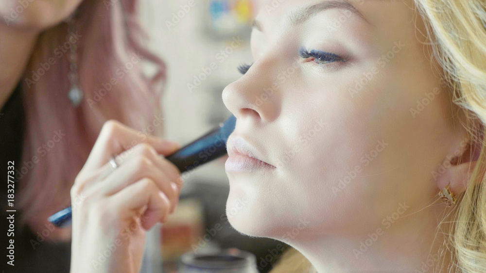 Young makeup artist applying concealer on model's face. Young makeup artist applying concealer on model's face.