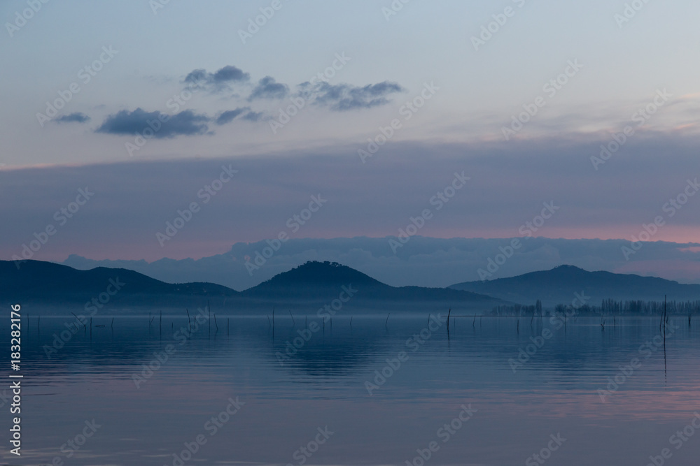 A lake at dusk, with beautiful, warm tones in the sky and water reflections, distant mountains, hills and trees