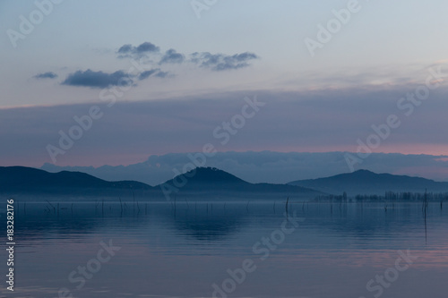 A lake at dusk, with beautiful, warm tones in the sky and water reflections, distant mountains, hills and trees